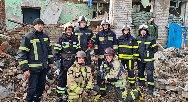 Lena ihop med ukrainska brandmän, en gruppbild framför en raserad byggnad där de rensat bland bråten.
