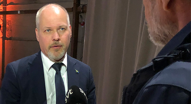 justitie- och inrikesminister Morgan Johansson blir intervjuad. Reportern står med ryggen mot kameran och sträcker fram en mikrofon mot ministern.