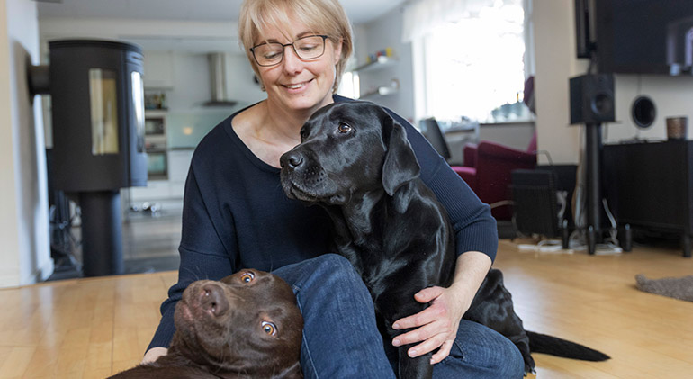 Eva Ladberg sitter på golvet i sitt vardagsrum och kelar med två större hundar.