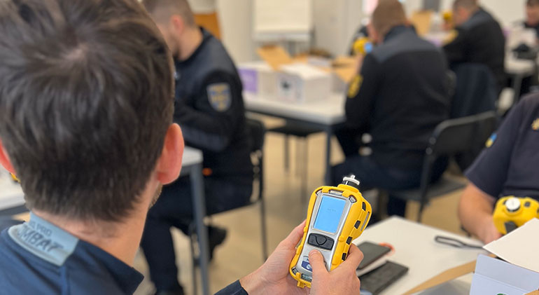 Personer från ukrainska räddningstjänster sitter i ett klassrum. Mannen närmast i bild håller i en gul gasdetektor.