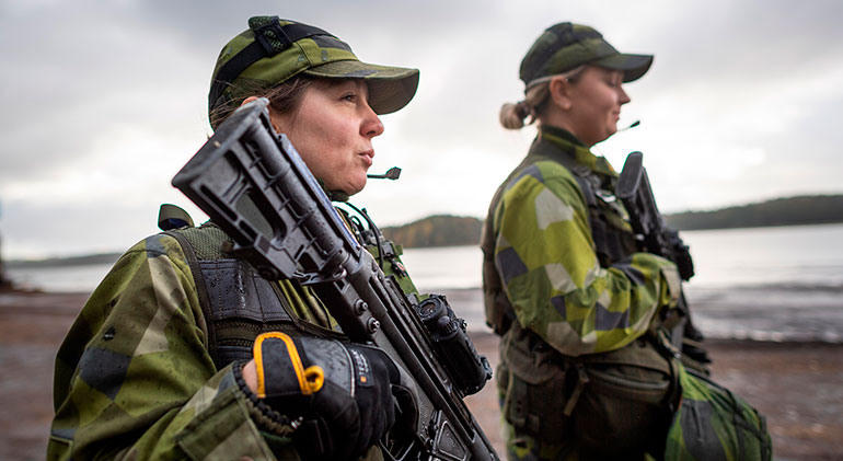 Två kvinnor från Hemvärnet håller i varsitt vapen och tittar ut över havet.