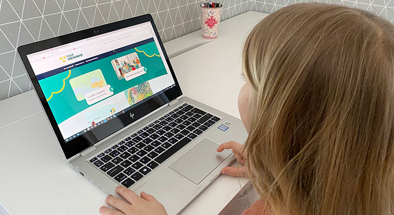 Flicka med långt hår sitter och tittar på webbplatsen Lilla Krisinfo på en laptop vid ett vitt skrivbord.