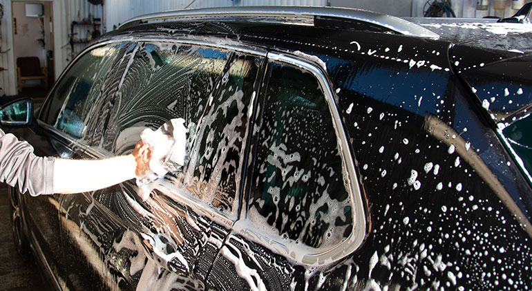 En arm som tvättar en bilruta med en tvättlapp. Bilen är svart och full med rengöringslödder.