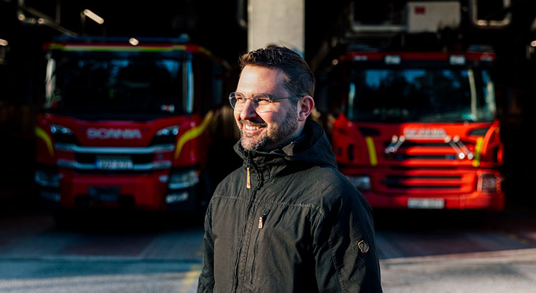 Brandingenjören och doktoranden Mateusz Sosnowski  står framför ett garage med två brandbilar.