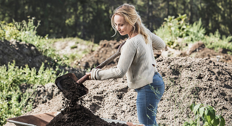 Liselotte Roll gräver i jorden med en stor spade och slänger jorden i en skottkärra.