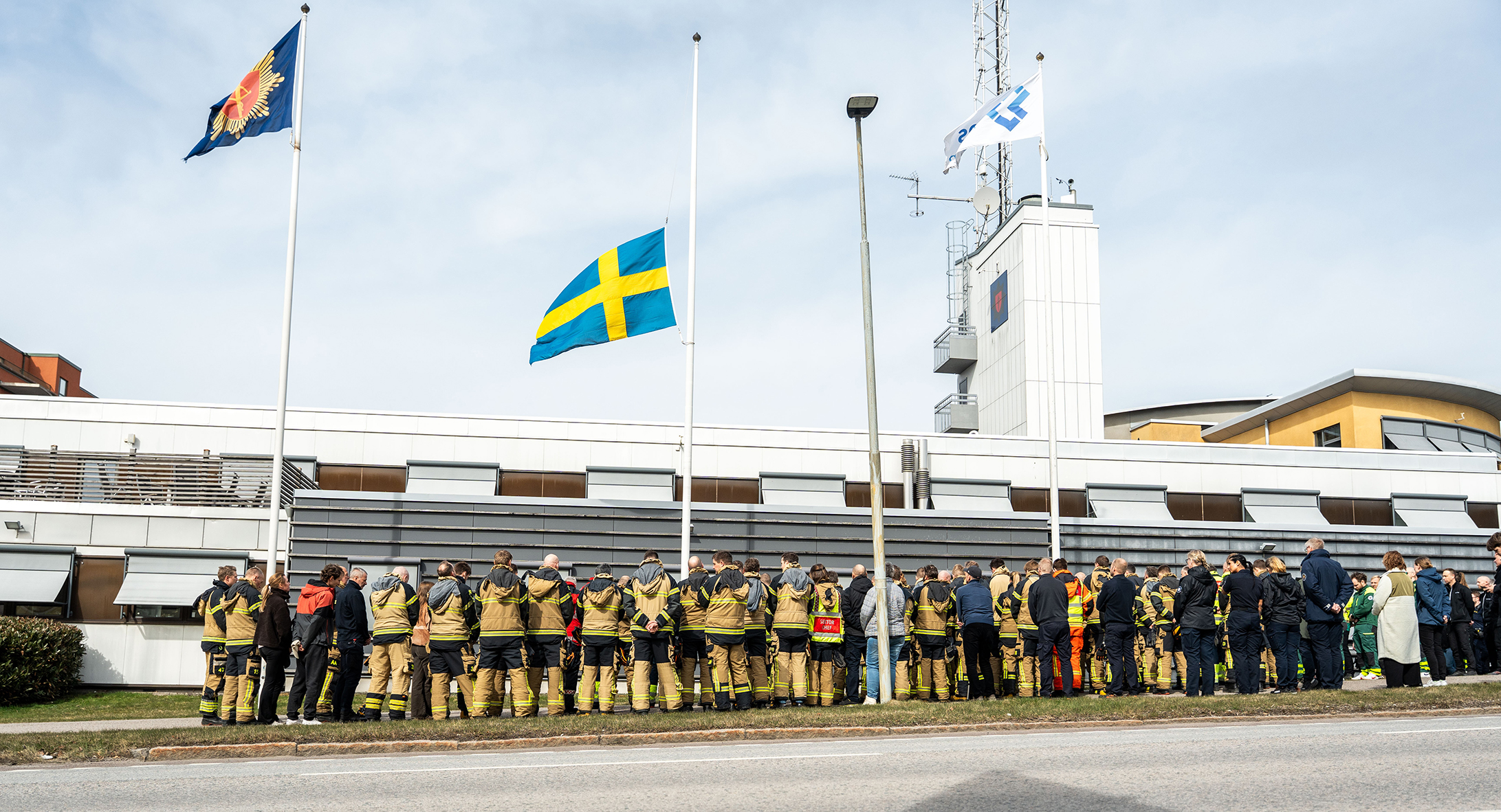Sörjande brandmän vid en flagga på halv stång